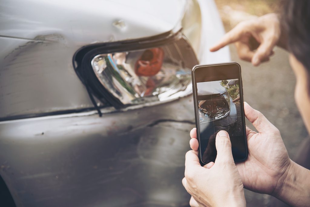 Persona haciendo una foto de los daños de un coche con un smartphone, lo que ilustra la importancia de documentar los daños personales para las reclamaciones al seguro.
