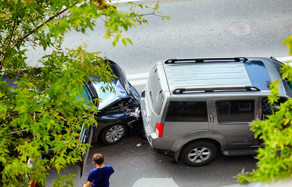 Vista aérea de una colisión por alcance entre un coche negro y un todoterreno gris en una calle de la ciudad, con un transeúnte cerca.