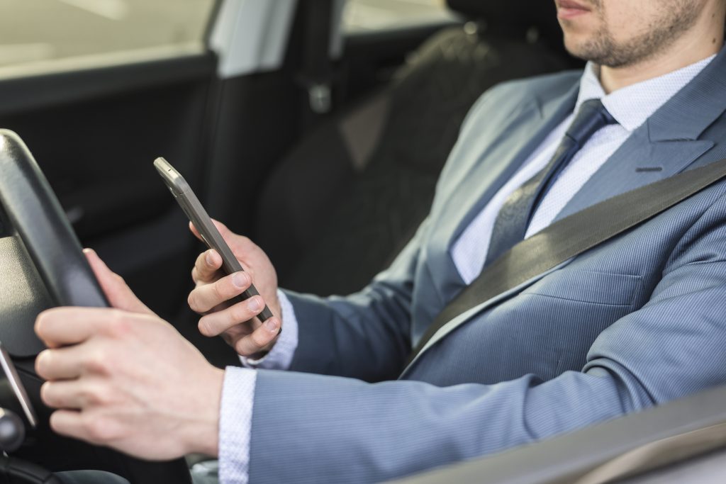 Driver in a suit using a smartphone behind the wheel, illustrating the dangers of texting and driving and the need for legal support in Decatur, GA after accidents.